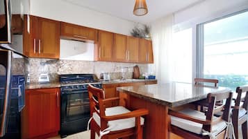 A modern kitchen with wooden cabinets, a gas stove, a built-in oven, and a granite countertop. There is a dining area with wooden chairs and a large window.