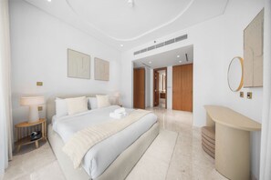 Ein modernes Hotelzimmer mit einem großen Bett, Nachttischen, einem Spiegel und einem durch eine offene Tür einsehbaren Badezimmer.