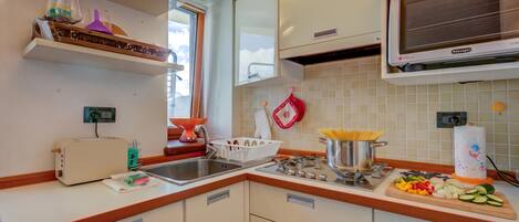 A kitchen with a built-in microwave, a stove, and a sink. There are cabinets, a toaster, and a window with a view of the sky.