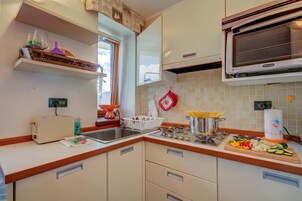 Una cocina con microondas incorporado, estufa y lavabo. Hay armarios, un tostador y una ventana con vistas al cielo.