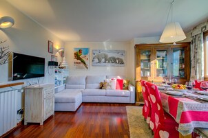 Una sala de estar con sofá, televisión y comedor con mesa lista para dos.