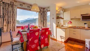 Ein Essbereich mit Tisch für zwei Personen, eine Küche mit Mikrowelle und Blick auf Berge durch große Fenster.