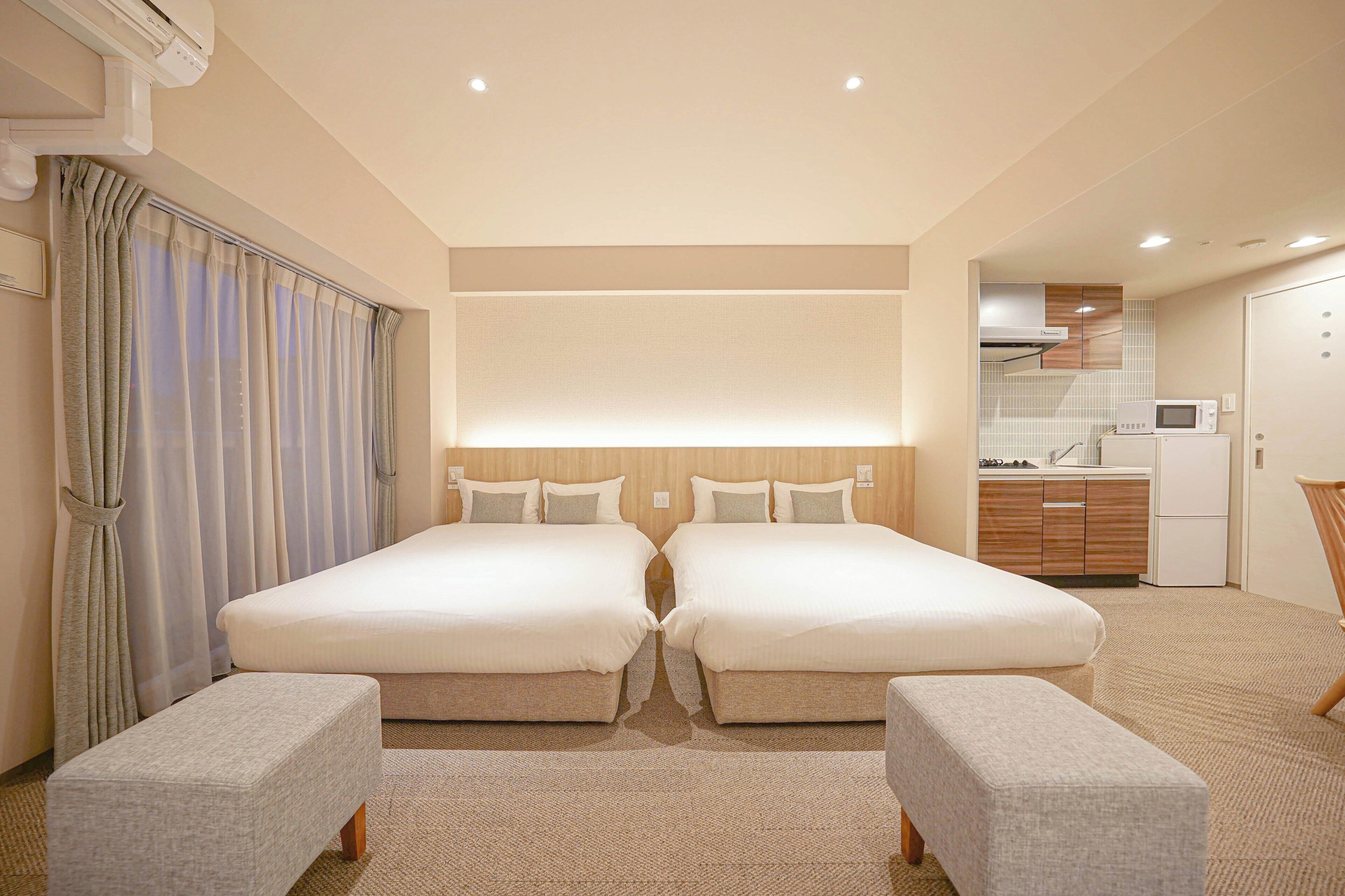 A hotel room with two beds, a kitchenette, and a bathroom.