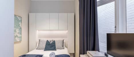 Habitación de hotel con cama, televisor de pantalla plana, impresora y ventana con cortinas.