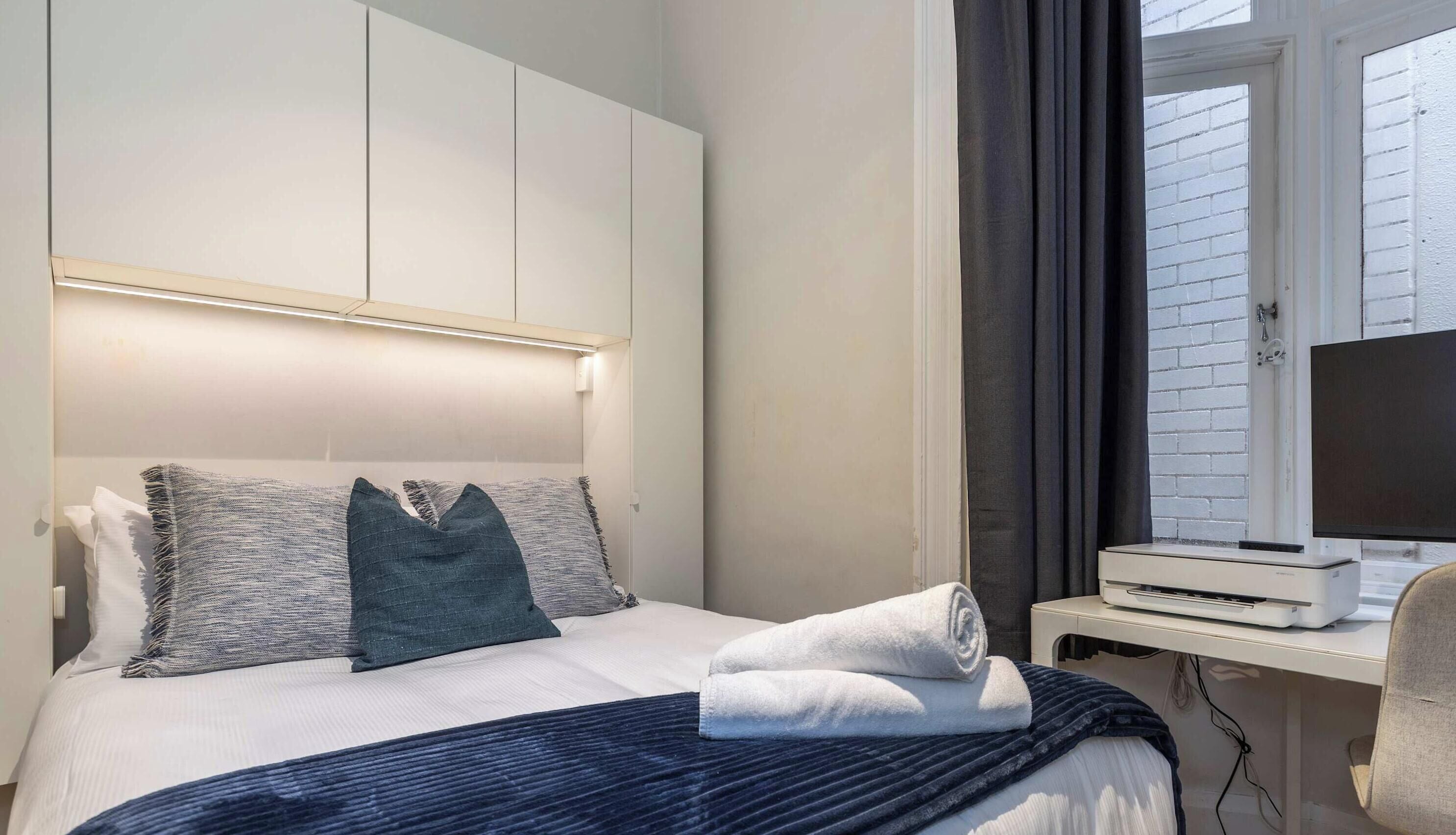 Hotelkamer met een bed, een flatscreen televisie, een bureau met een printer en een raam met jaloezieën.