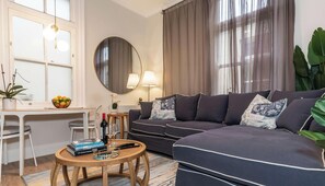 A living room with a sofa, a round coffee table, a dining table with chairs, a mirror, and a window with curtains. - 3BR Art Deco Retreat in the Heart of Potts Point (Potts Point)
