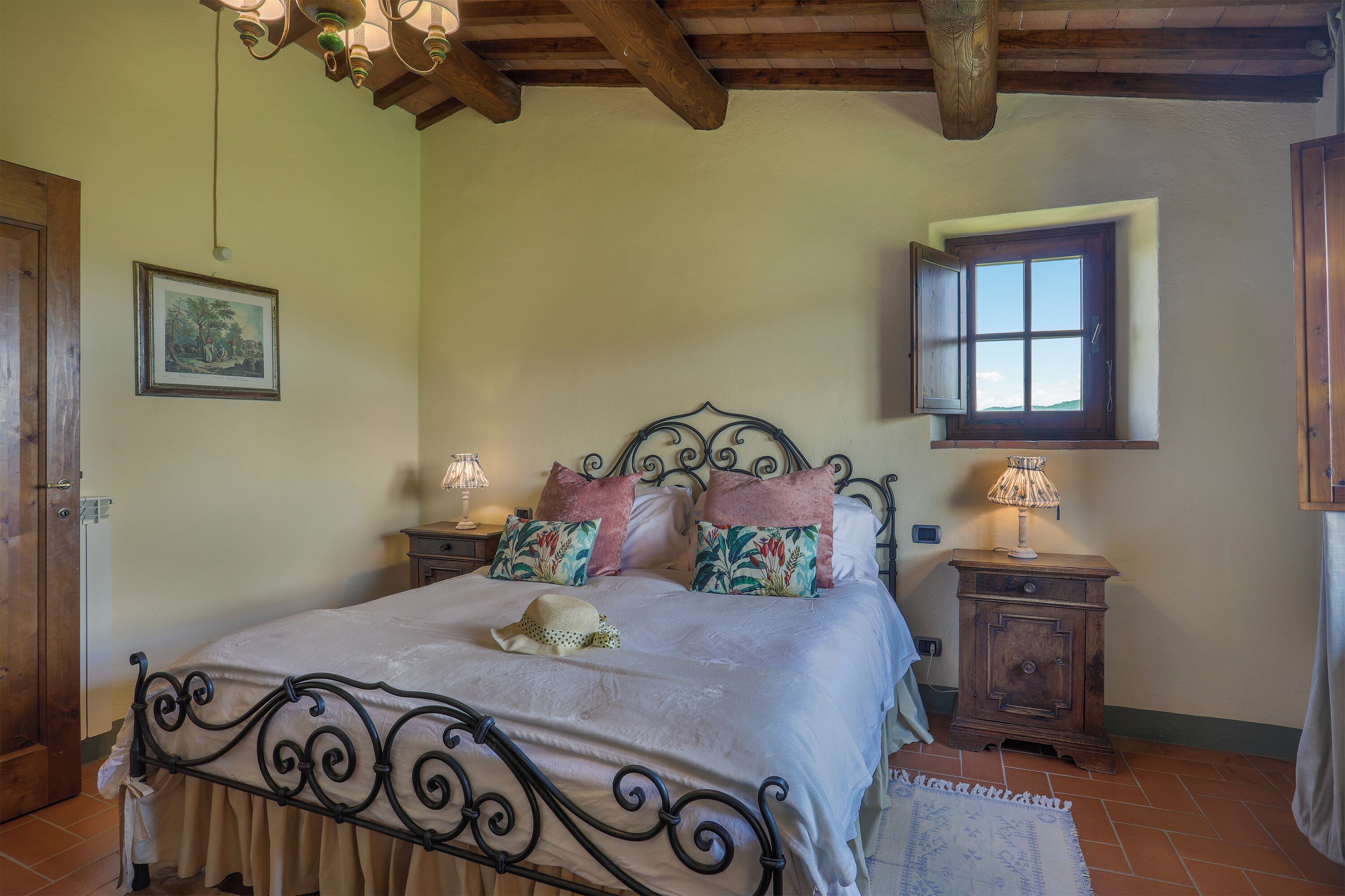 A bedroom with a bed, two bedside tables, a window, a picture on the wall, and a door.