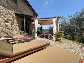 A stone building with a patio area featuring lounge chairs and a table. - Casa Poggio in Badia in the Chianti Shire (Toscana)