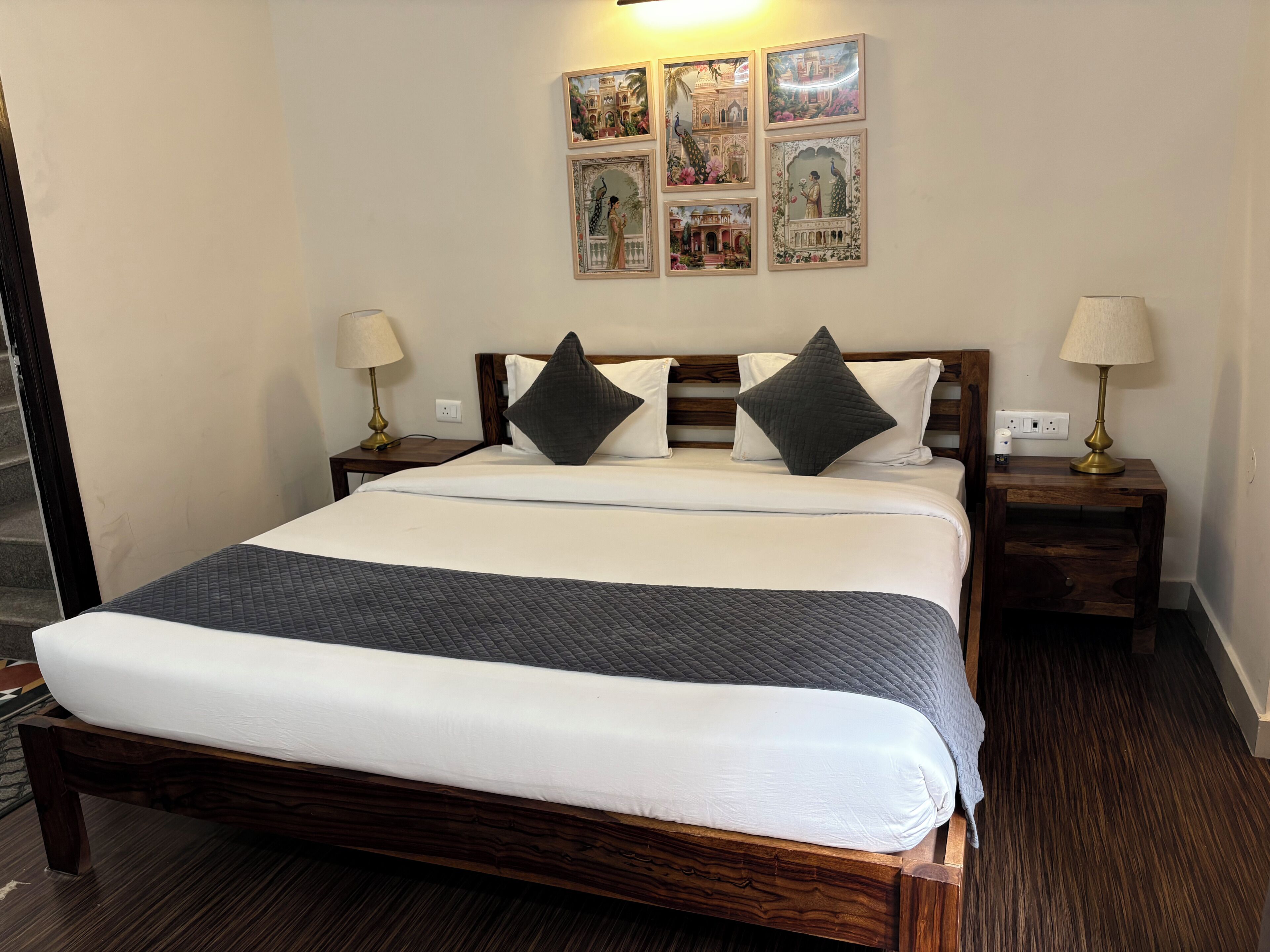 A neatly made bed with a dark quilt, two bedside lamps, and a wall with framed pictures.