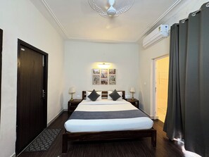 A hotel room with a bed, two bedside tables, a ceiling fan, wall-mounted artwork, and an air conditioning unit.