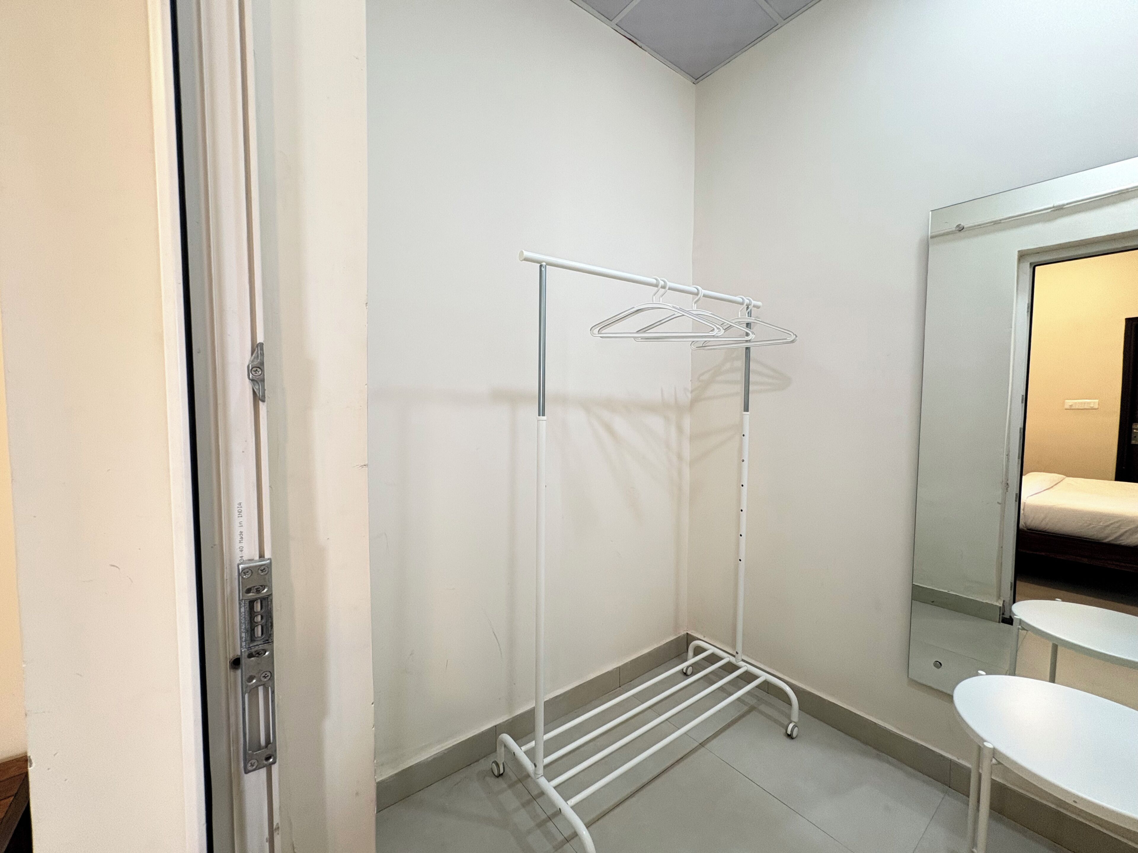 A room with a white metal drying rack, a small white table, and a mirror on the wall.