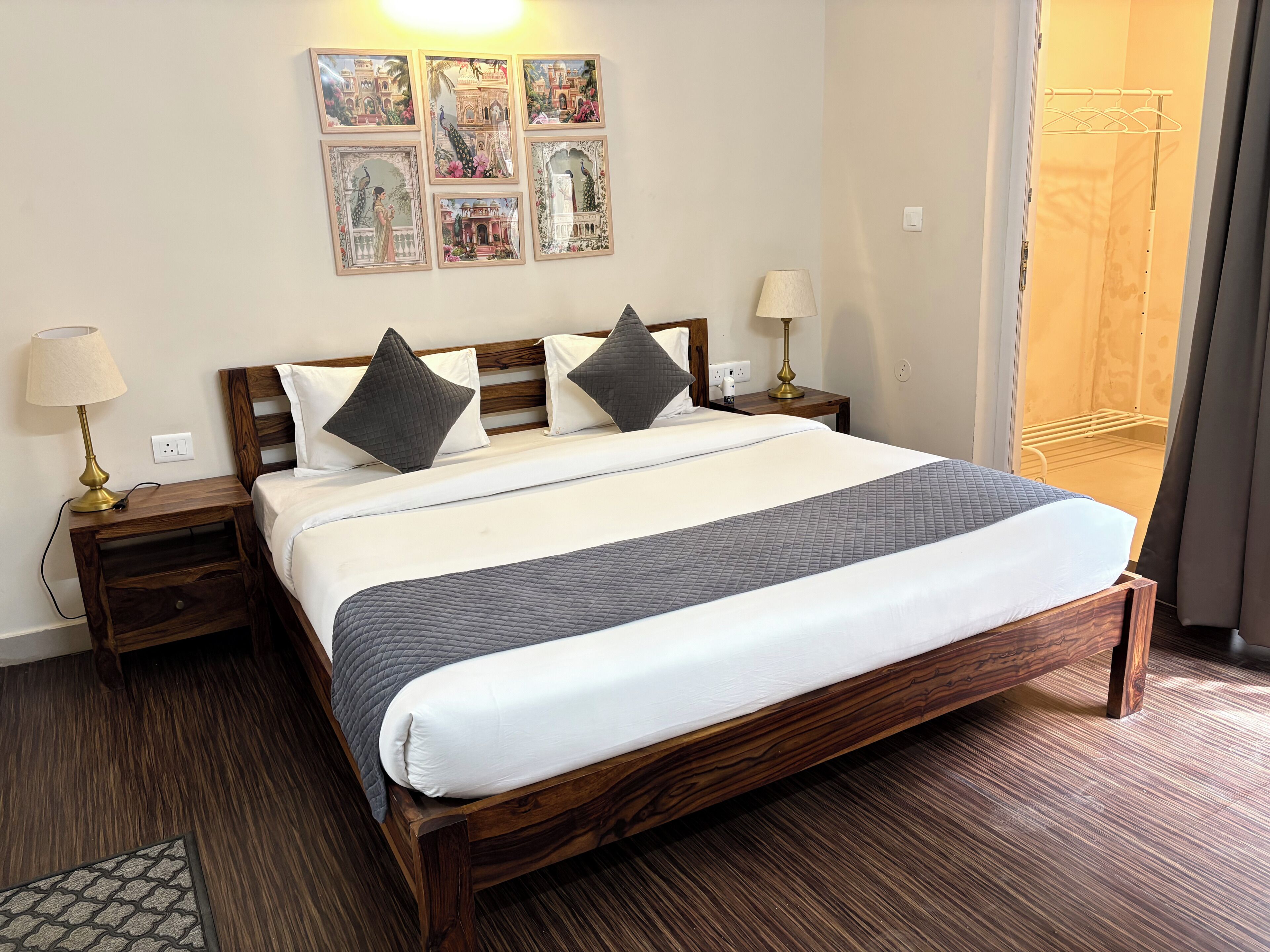 A hotel room with a large bed, two bedside tables, a lamp, a wall-mounted picture, and a door leading to another room.