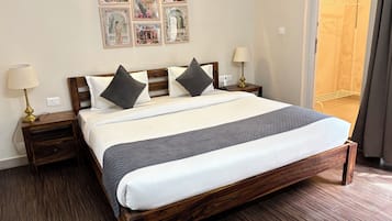 A hotel room with a large bed, two bedside tables, a lamp, a wall-mounted picture, and a door leading to another room.