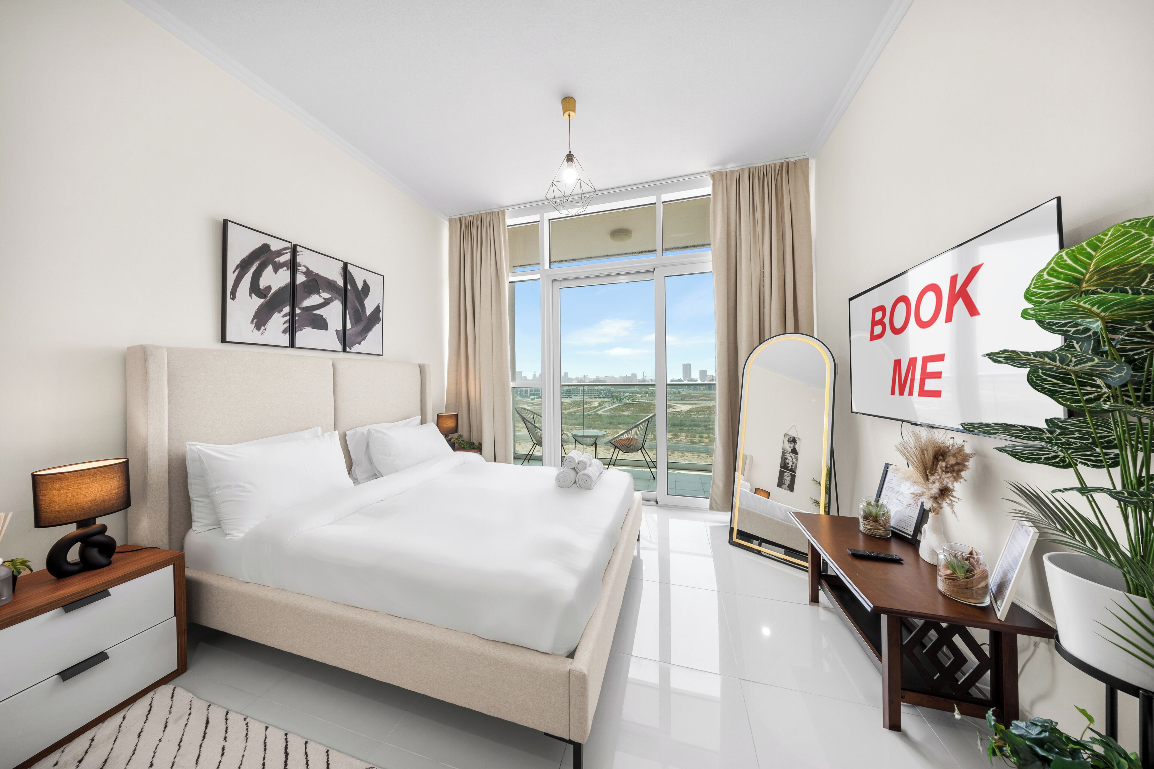 A modern hotel room with a large bed, a desk, a chair, a large window with a city view, and a 'BOOK ME' sign.