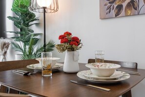 A dining table with a vase of red flowers, a glass of amber liquid, and a plate with a floral pattern. - StayShort - Cozy Studio in DAMAC Hills that Sleeps 2 (Damac Hills 1)