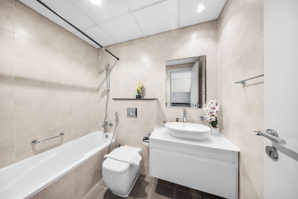 A modern bathroom with a bathtub, toilet, sink, and shower. - StayShort - Cozy Studio in DAMAC Hills that Sleeps 2 (Damac Hills 1)