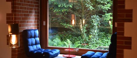 A room with a large window, two blue chairs, a small red table, and a hanging light fixture.