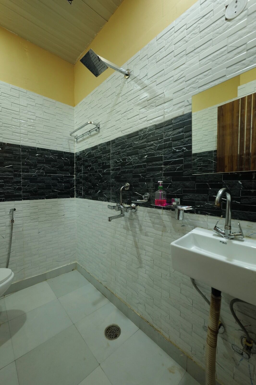 Un baño con paredes de azulejos blancos y negros, ducha, dos lavamanos y un inodoro.