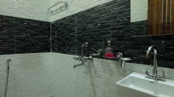 Un baño con paredes de azulejos blancos y negros, ducha, dos lavamanos y un inodoro.