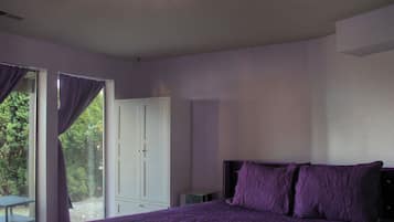 A bedroom with a bed, a window with curtains, a door, and a small table.