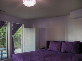 Un dormitorio con cama, una ventana con cortinas, una puerta y una mesita.