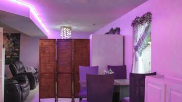 A dining area with a table and chairs, a wooden cabinet, and a purple-lit ceiling.