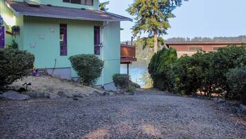 A house with a gravel driveway, a wooden deck, and a view of a lake.