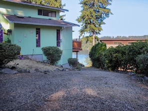 Una casa con camino de grava, terraza de madera y vista al lago.