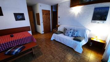 Una stanza con un letto, un divano, un tavolo con tovaglia a quadri rossi e una lampada fissata al muro.