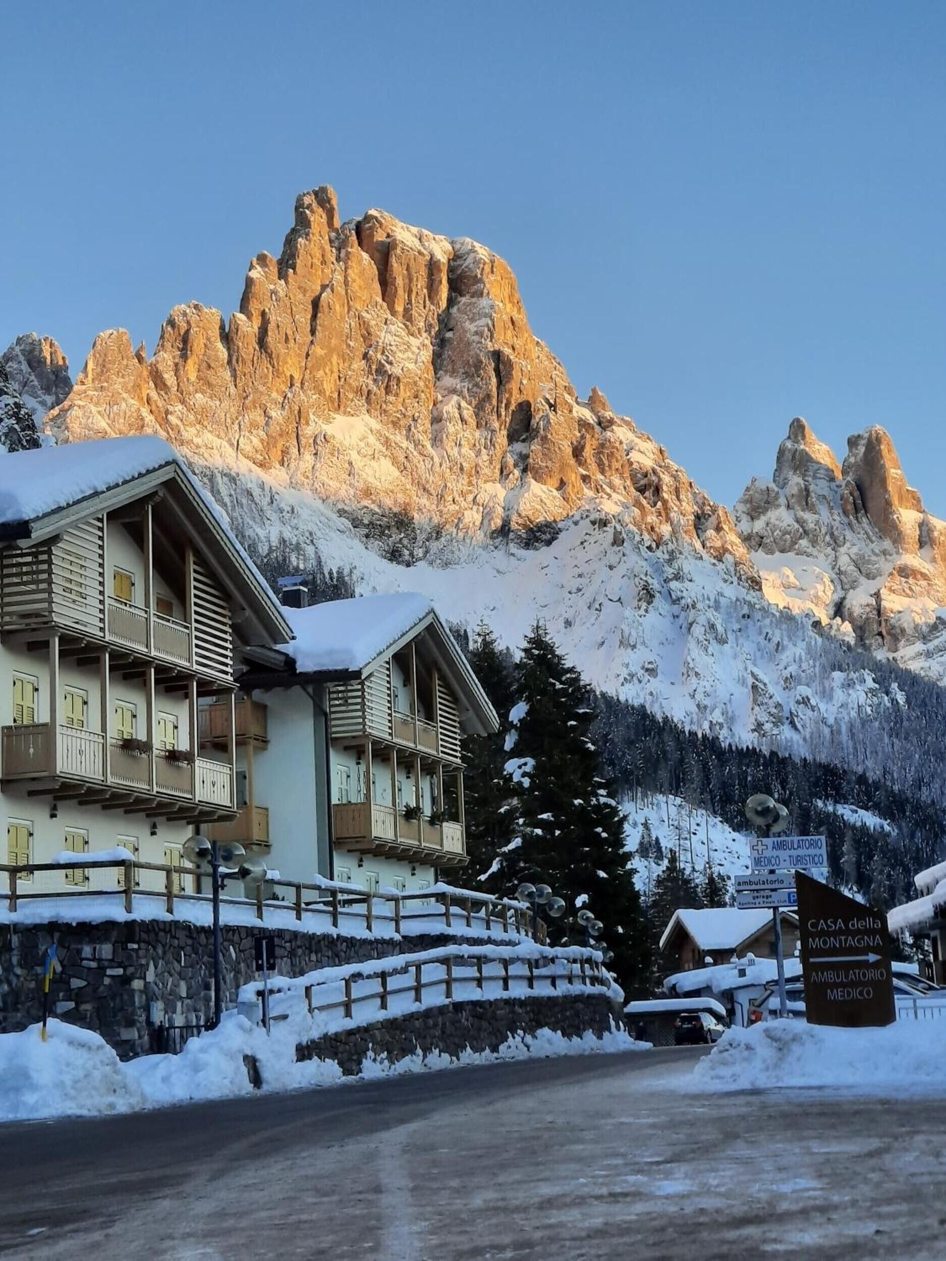 Un hotel con le montagne sullo sfondo, con un balcone innevato e un cartello che indica una struttura medica.