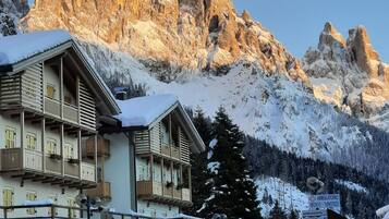 Un hotel con le montagne sullo sfondo, con un balcone innevato e un cartello che indica una struttura medica.