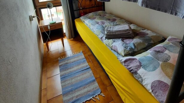A small, cozy room with a bunk bed, a window with curtains, a wooden floor, and a striped rug. - Apartment 'Stregatto Dalla Luna - Dolomiti' with Mountain View, Private Terrace and Wi-Fi (San Martino di Castrozza)