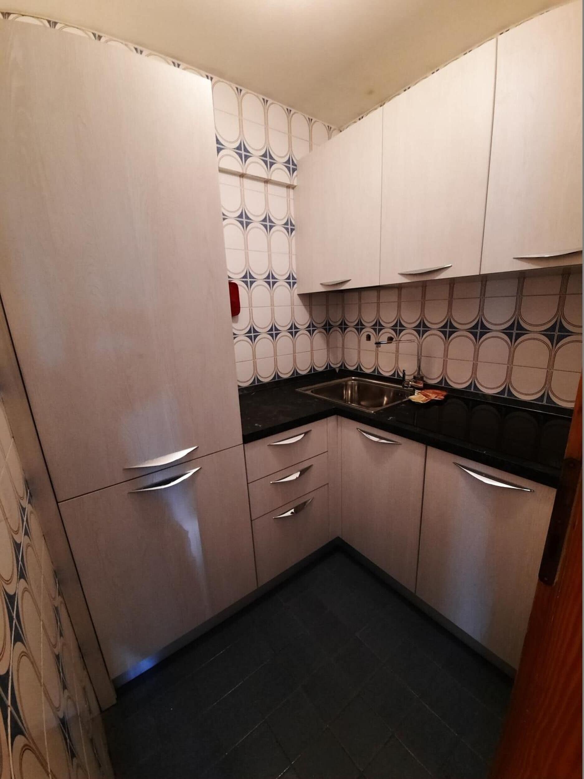 Una cucina con mobili chiari, un piano di lavoro nero e un backsplash decorato.