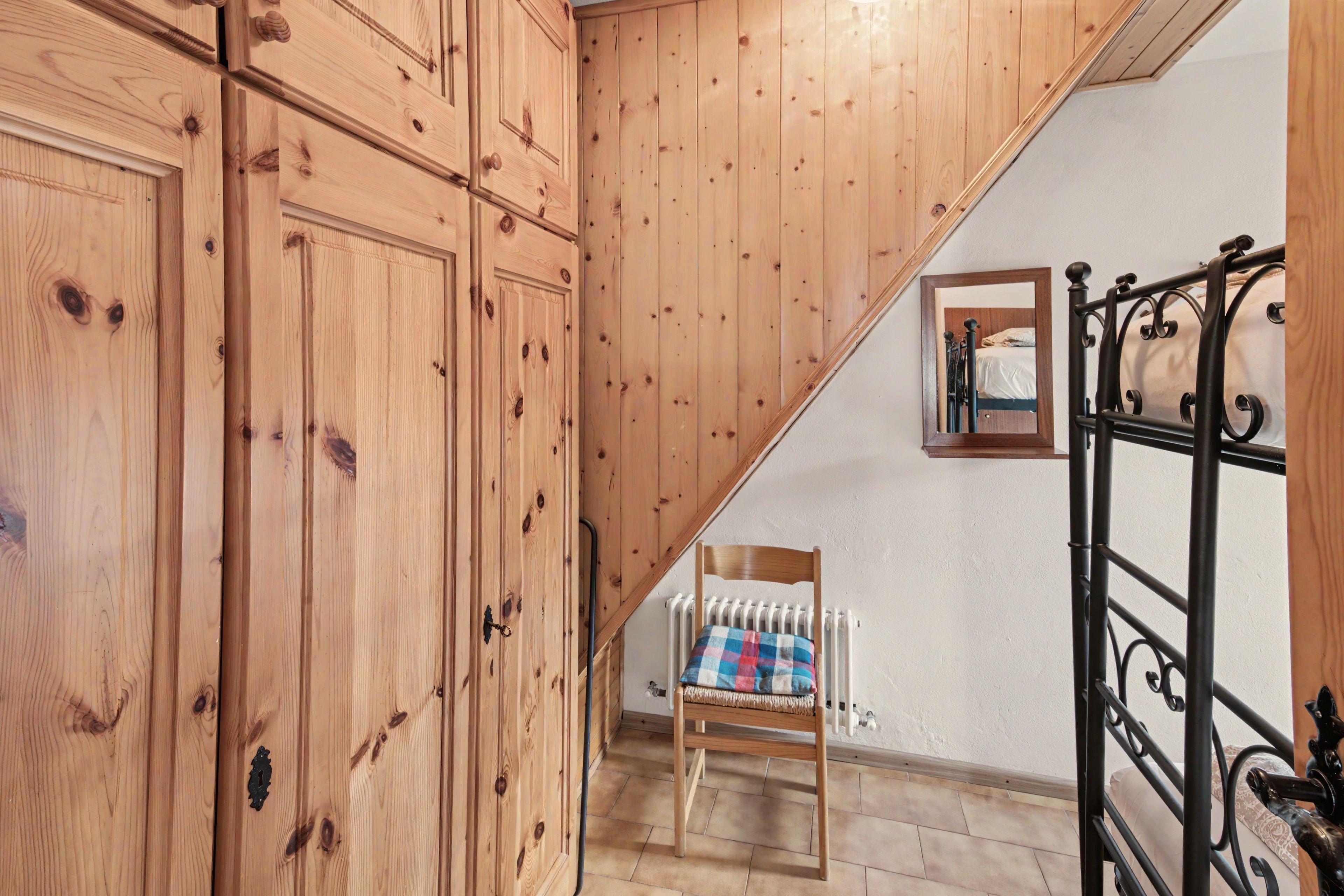 Una scala in legno conduce a una camera da letto con un letto, una sedia e un termosifone.