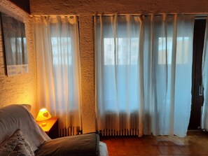 A room with a bed, a nightstand with a lamp, and sheer curtains. - Apartment 'Stregatto Dalla Luna - Dolomiti' with Mountain View, Private Terrace and Wi-Fi (San Martino di Castrozza)