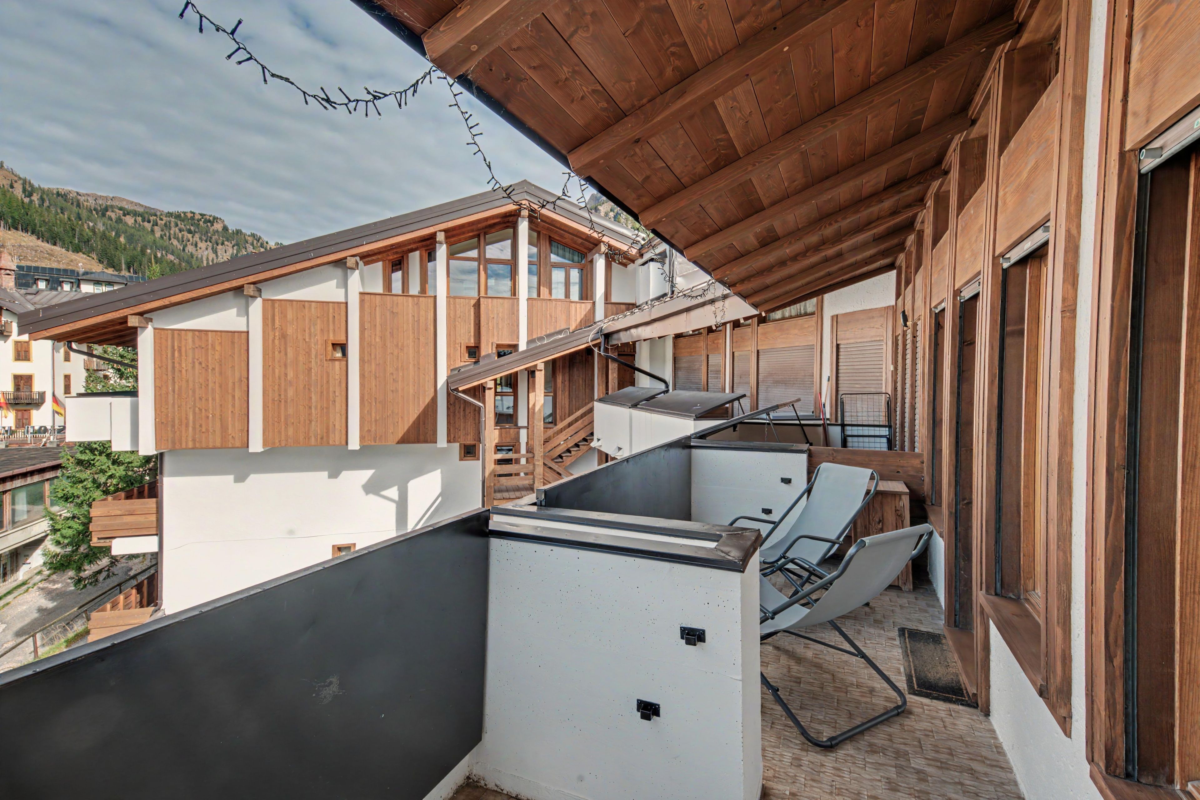 Un bâtiment moderne à l’extérieur en bois, doté d’un balcon avec une chaise en métal, et offrant une vue sur les environs.
