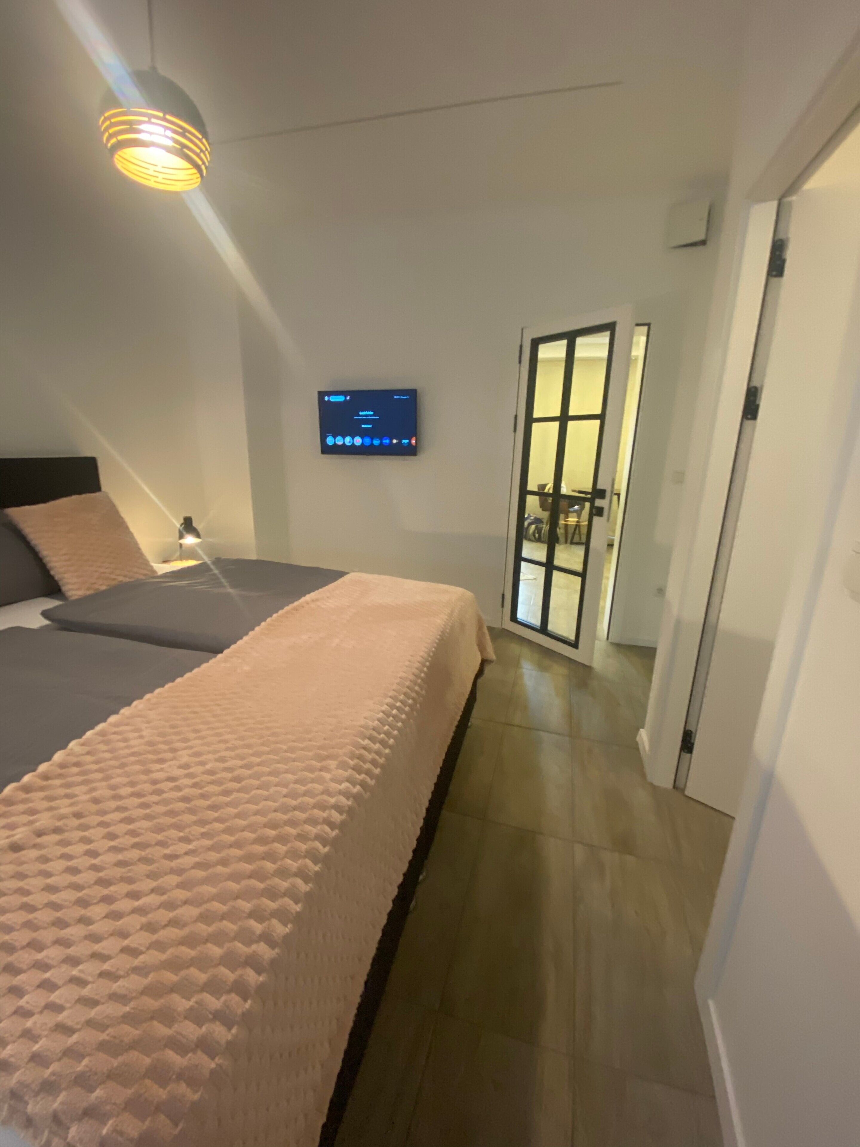 A modern bedroom with a bed, bedside lamp, and a television on the wall.