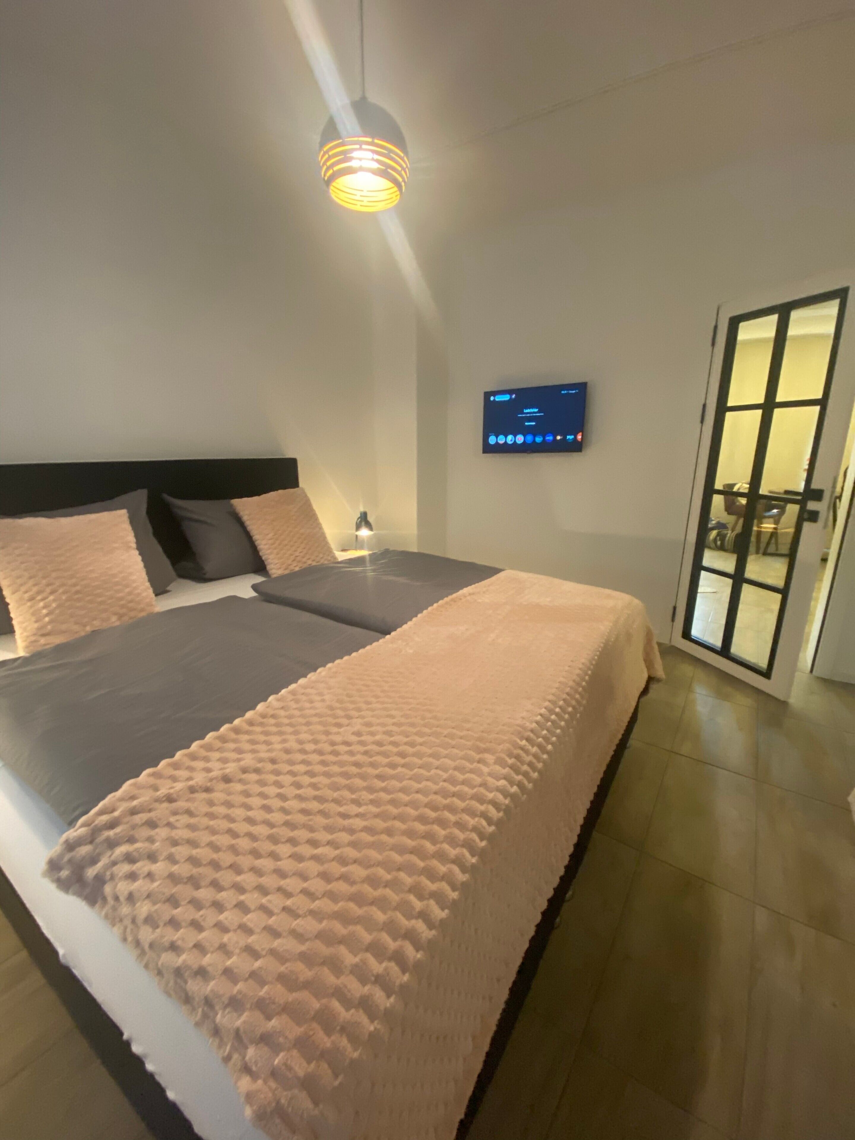 Une chambre moderne avec un lit, un téléviseur fixé au mur et une porte donnant sur un balcon.