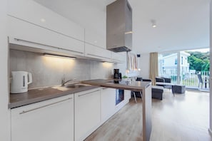 A modern kitchen with a built-in oven, a coffee maker, and a kettle. - Dünenvilla 10, Apartment 04 (Lübeck-Travemünde)