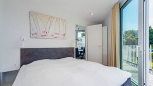 Un dormitorio moderno con una cama grande, una lámpara de techo, una obra de arte colgada en la pared y vistas al exterior a través de una puerta corredera.