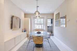 A dining area with a round table, chairs, a hanging light fixture, and a patterned rug. - The Weaver of Westbourne Green, by Veeve (London)
