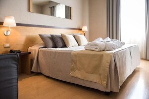 Una habitación de hotel con cama, lámparas de noche, teléfono y espejo en la pared.