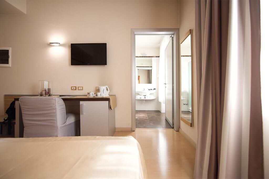 A hotel room with a bed, a desk, a television, and a bathroom visible through an open door.