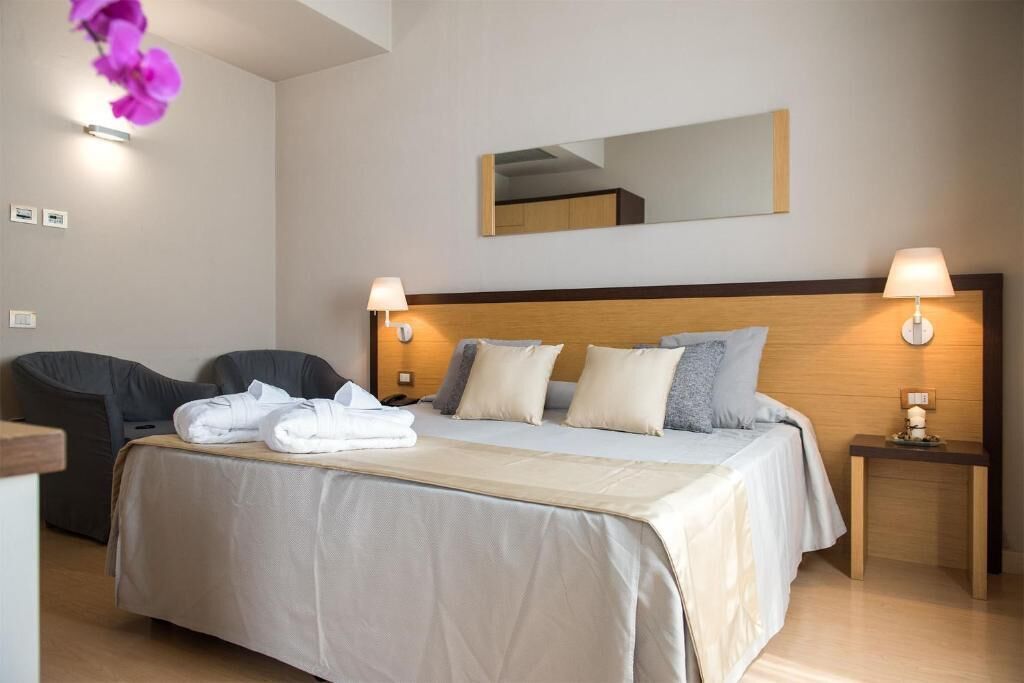 Une chambre d’hôtel avec un lit, deux tables de chevet, une chaise et un miroir au mur.