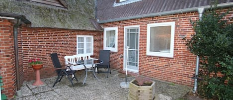 Una casa de ladrillo con un patio, una mesa, sillas y una planta en maceta.