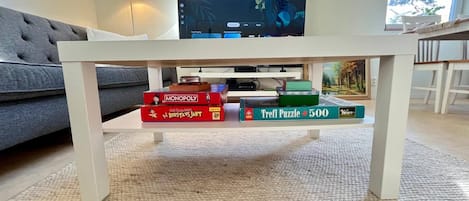 Ein Wohnzimmer mit einem weißen Couchtisch, auf dem Gesellschaftsspiele und ein Fernseher stehen.