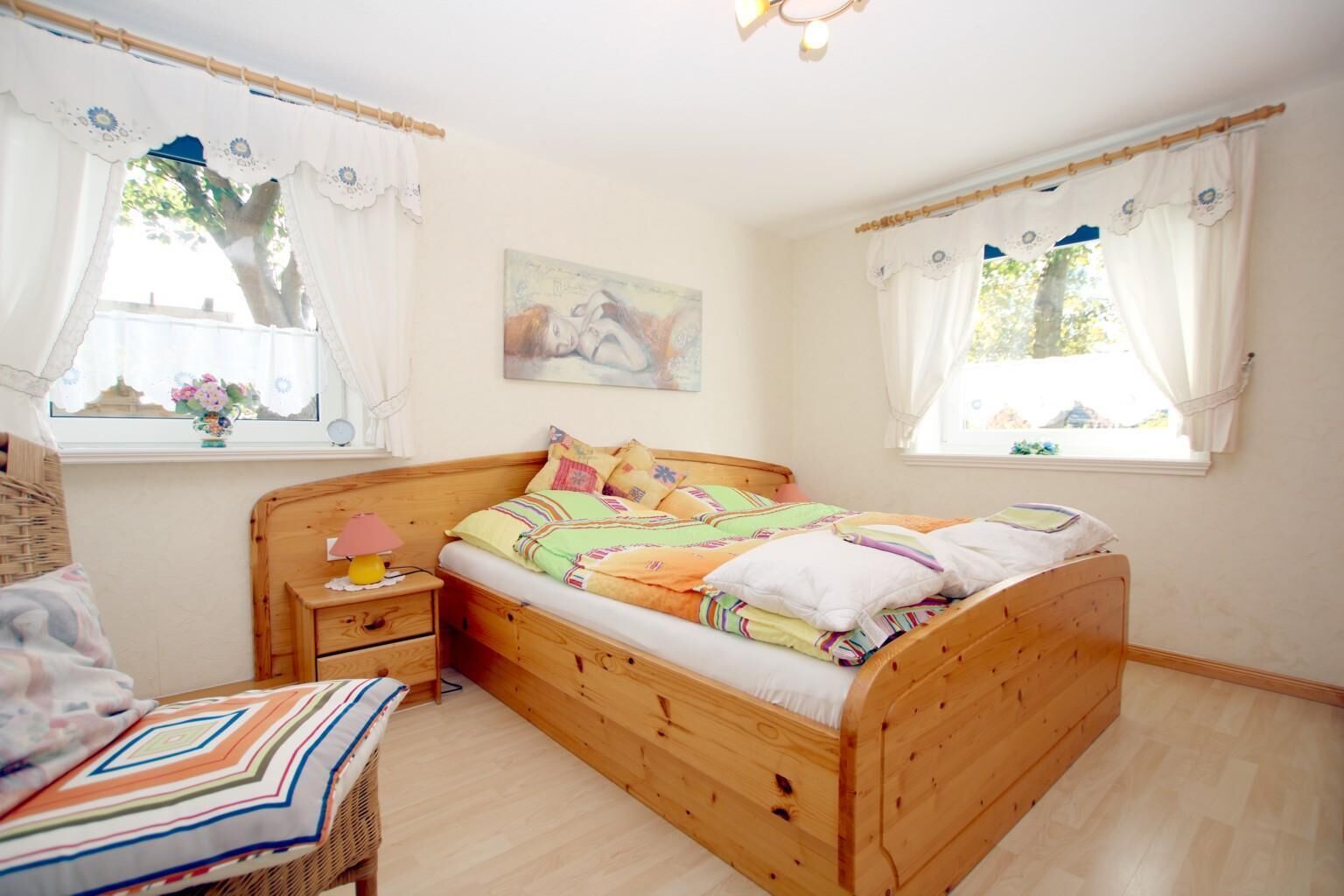 A cozy bedroom with a wooden bed, a bedside table, a chair, and a window with curtains.