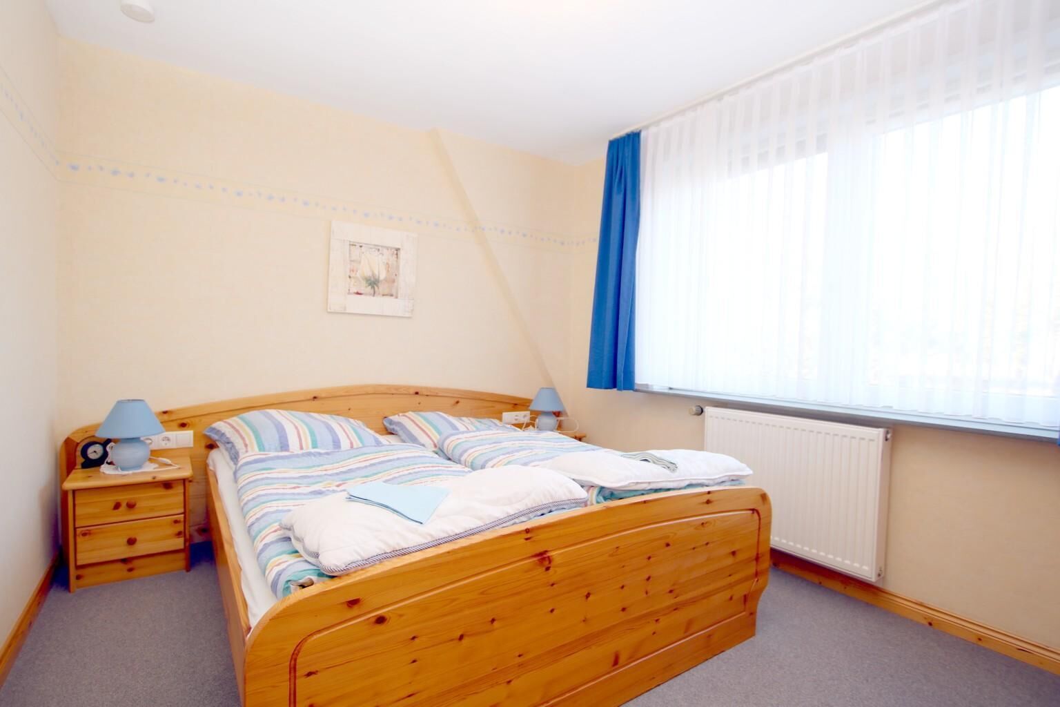 Een slaapkamer met een houten bed, nachtkastjes, een raam met gordijnen en een radiator.