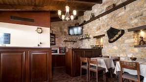 A rustic bar area with stone walls, wooden furniture, and a television mounted on the wall.
