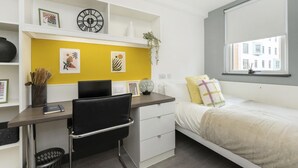 Quarto moderno com cama, escrivaninha e uma cadeira. Há uma janela com vista para edifícios.
